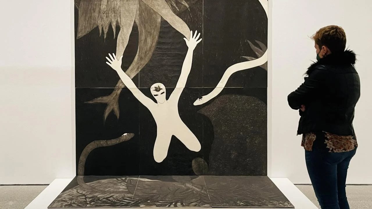 Sala del MALBA con una gran colografía de Belkis Ayón: una figura blanca con los brazos en alto entre serpientes, ante la que se detiene una visitante